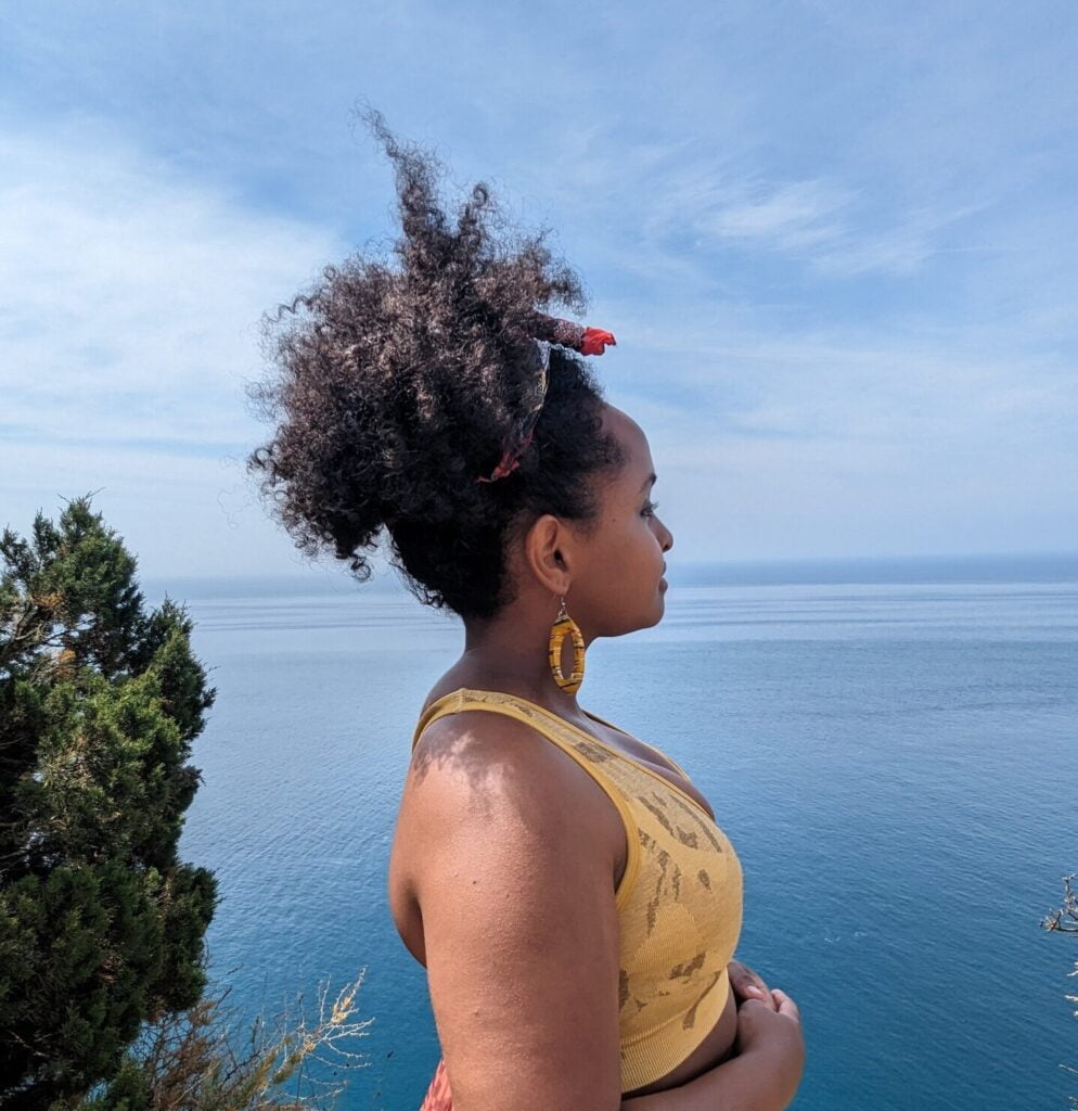 Side profile of a Black woman with tied up afro stares out into a blue sky and ocean in Portugal