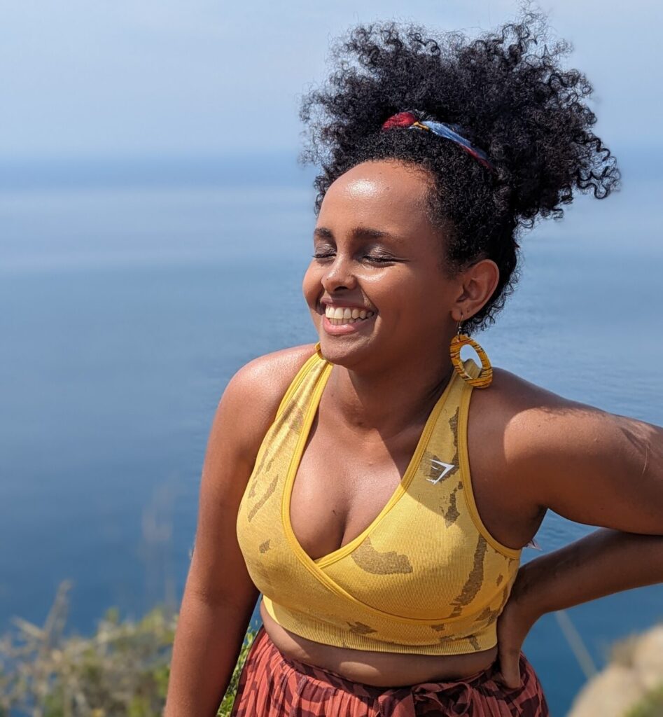Black woman with natural hair afro with a blue-sky background in a yellow sports bra laughing