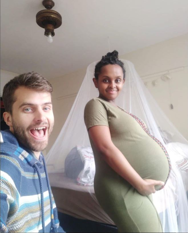 a black woman in a green dress heavily pregnant with twins next to her white husband