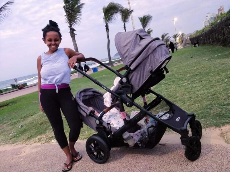 black mother with twin stroller near a beach