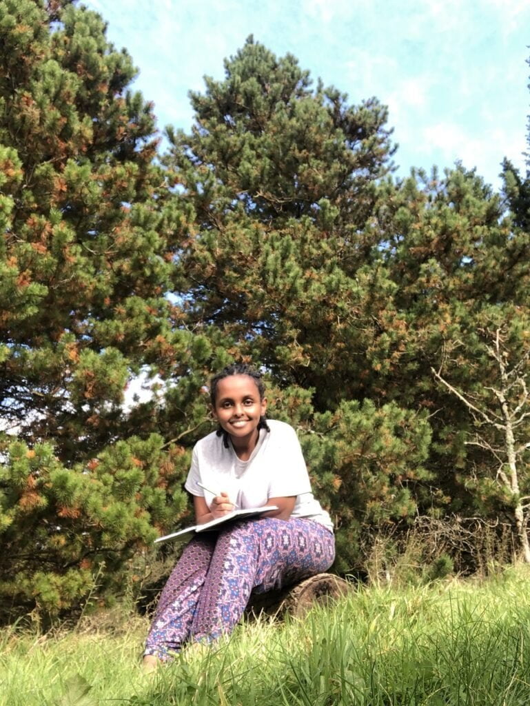 black woman in forest with an open book and pen