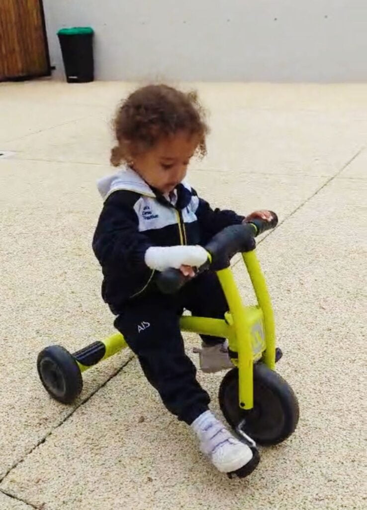 Toddler with a bandages finger riding a lime green bicycle