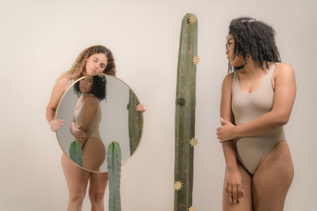 Black woman looking sadly into a mirror held up by a mixed-race woman.